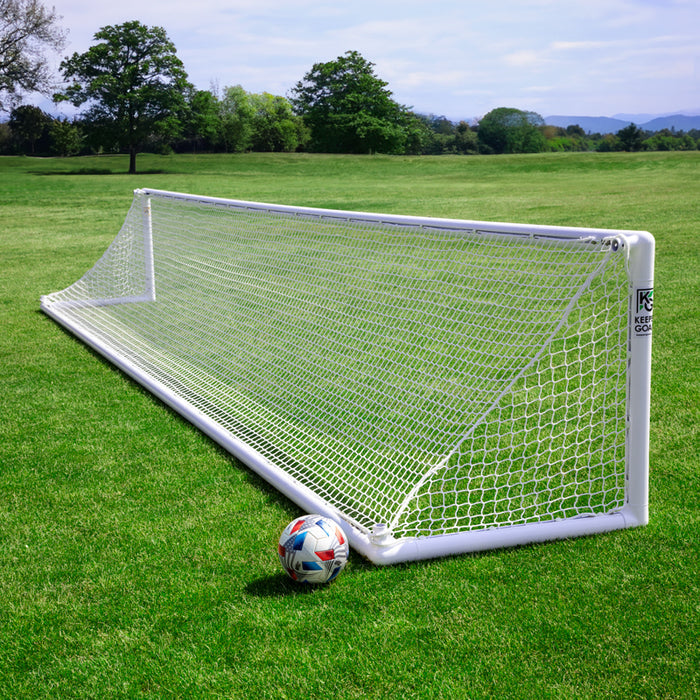 The Precizion Soccer Goal | 3' x 24' Aluminum Finishing & Training Goal with a white net stands on a grassy field under a blue sky. A soccer ball rests nearby, perfect for goalkeeper training amid trees and distant hills.
